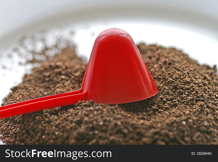 Macro closeup of a red conical coffee scoop with ground coffee poured onto a white plate. Macro closeup of a red conical coffee scoop with ground coffee poured onto a white plate