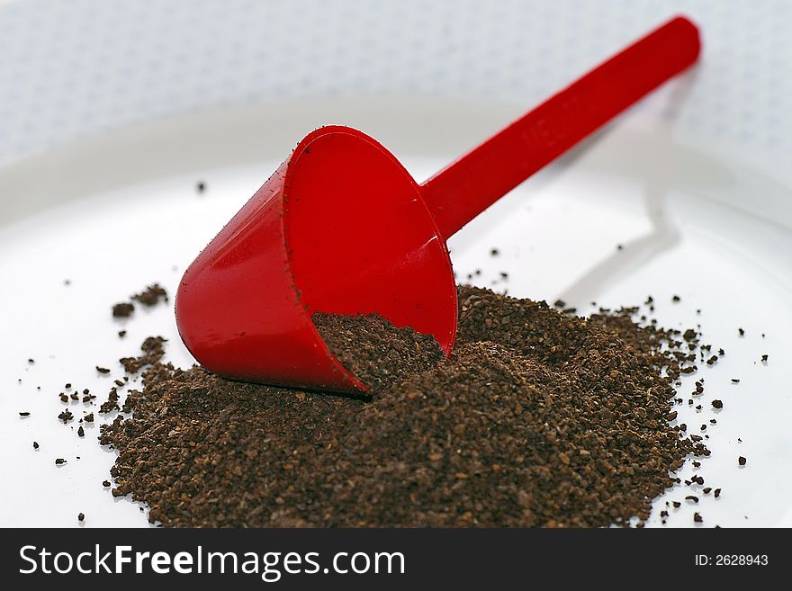 Macro closeup of a red conical coffee scoop with ground coffee poured onto a white plate. Macro closeup of a red conical coffee scoop with ground coffee poured onto a white plate