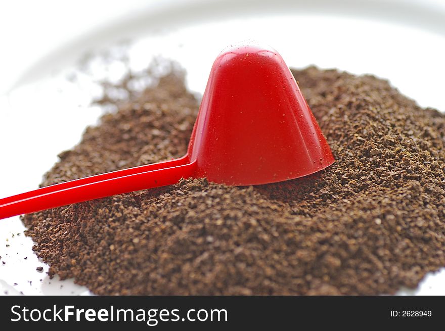 Macro closeup of a red conical coffee scoop with ground coffee poured onto a white plate. Macro closeup of a red conical coffee scoop with ground coffee poured onto a white plate