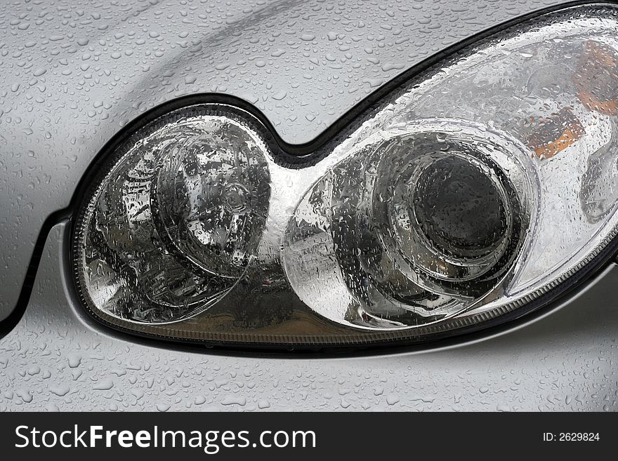 Shiny car with silver paint. Water drops on the hood. Car lamp.