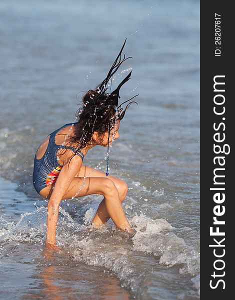 Pretty young girl has fun at the seafront. Her long hairs splashing waterdrops through the air