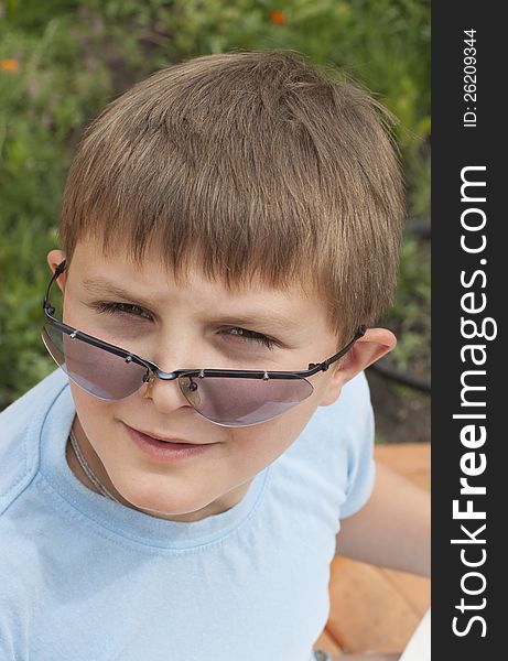 The boy (10 years) looks through sunglasses against a green lawn. The boy (10 years) looks through sunglasses against a green lawn