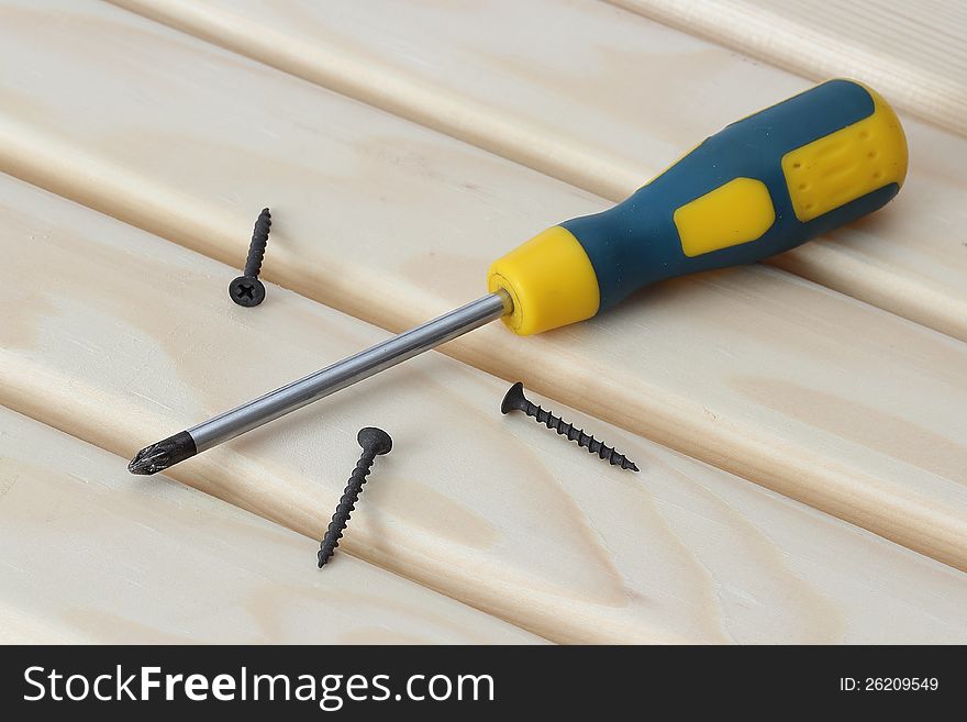 Screwdriver and three screws over wood