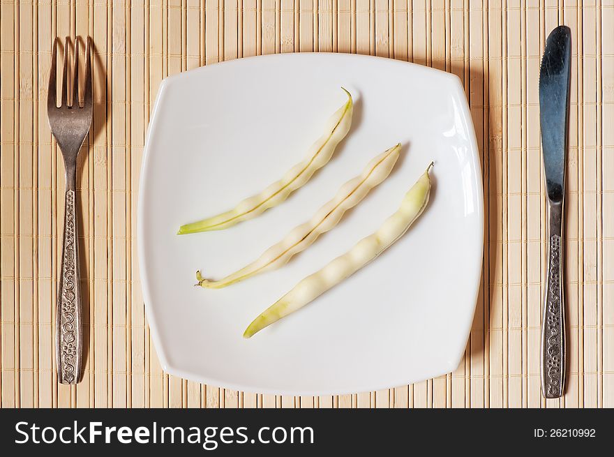 Three pods of beans on a white square plate. Three pods of beans on a white square plate.