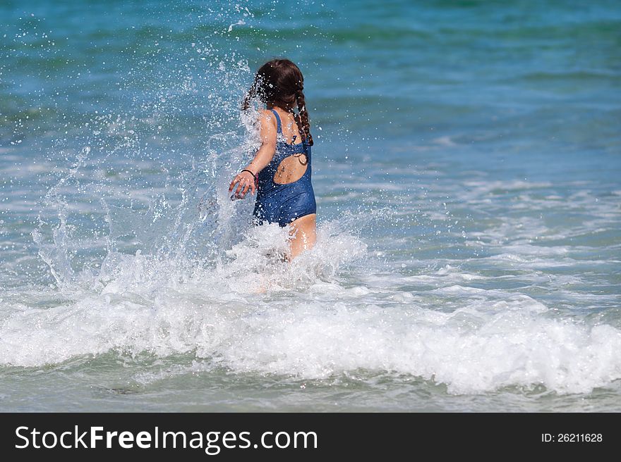 Cute young girl runs in the wave of the sea