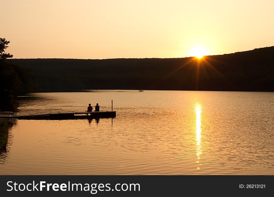 A couple sitting on a boat dock watching reflections on as the sun sinks over the mountain. A couple sitting on a boat dock watching reflections on as the sun sinks over the mountain.