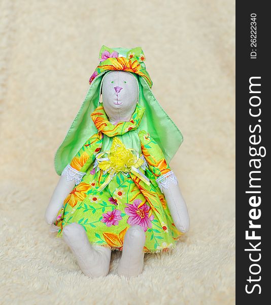 The doll a tilde hare in a green dress and a hat sits. The doll a tilde hare in a green dress and a hat sits