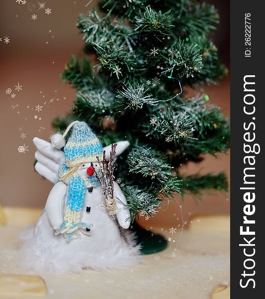 Toy angel a snowman in a blue cap under a fir-tree. Toy angel a snowman in a blue cap under a fir-tree