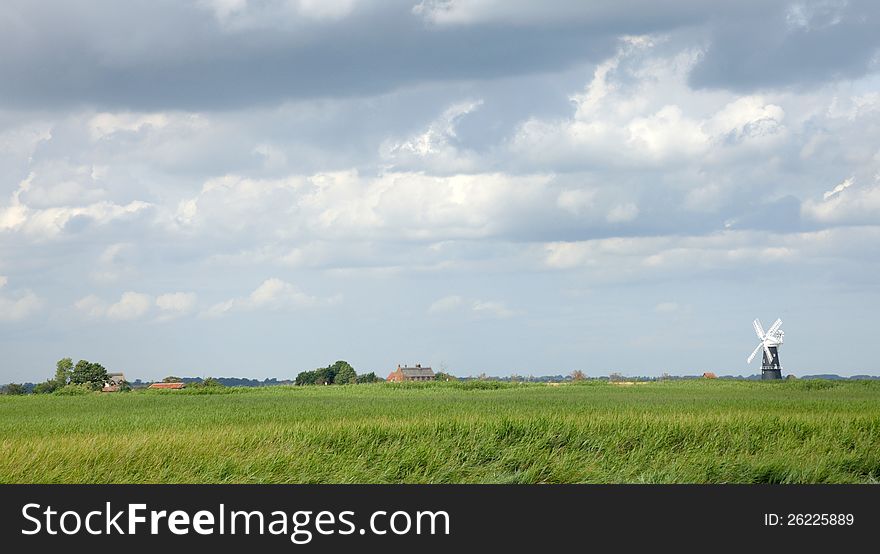 A windmill stands out from the flat landscape of the Norfolk Broads. England.
Green water meadows cloudy sky.