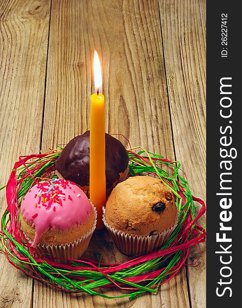 Three cupcakes and a burning candle on a wooden table