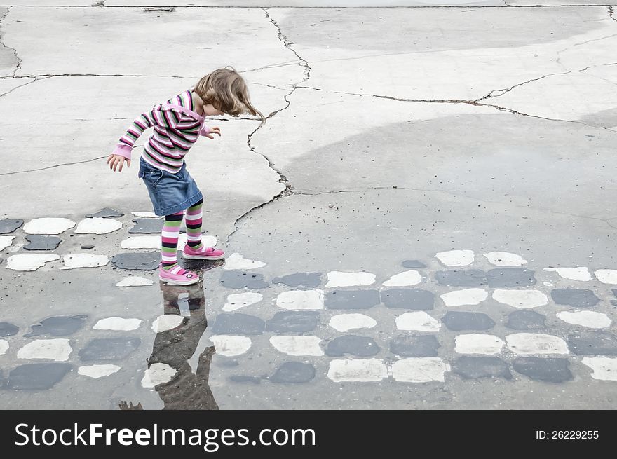 Young girl playing hopscotch on some old black and white tiles.