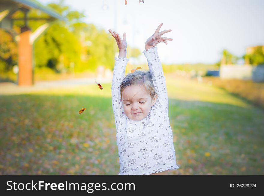 Pretty, young girl throwing leaves into the air while playing outside. Pretty, young girl throwing leaves into the air while playing outside.