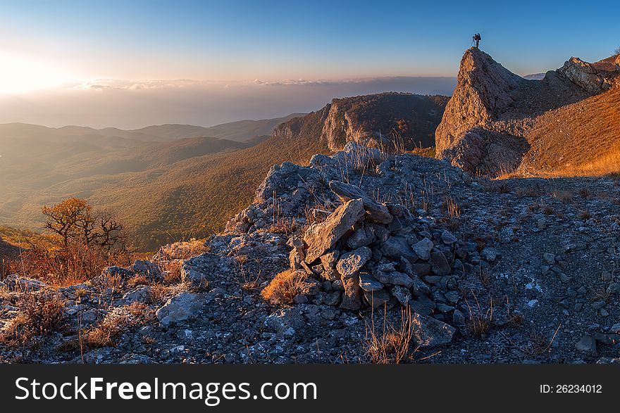 A man standing at mountain top with camera against a beautiful sunrise. A man standing at mountain top with camera against a beautiful sunrise