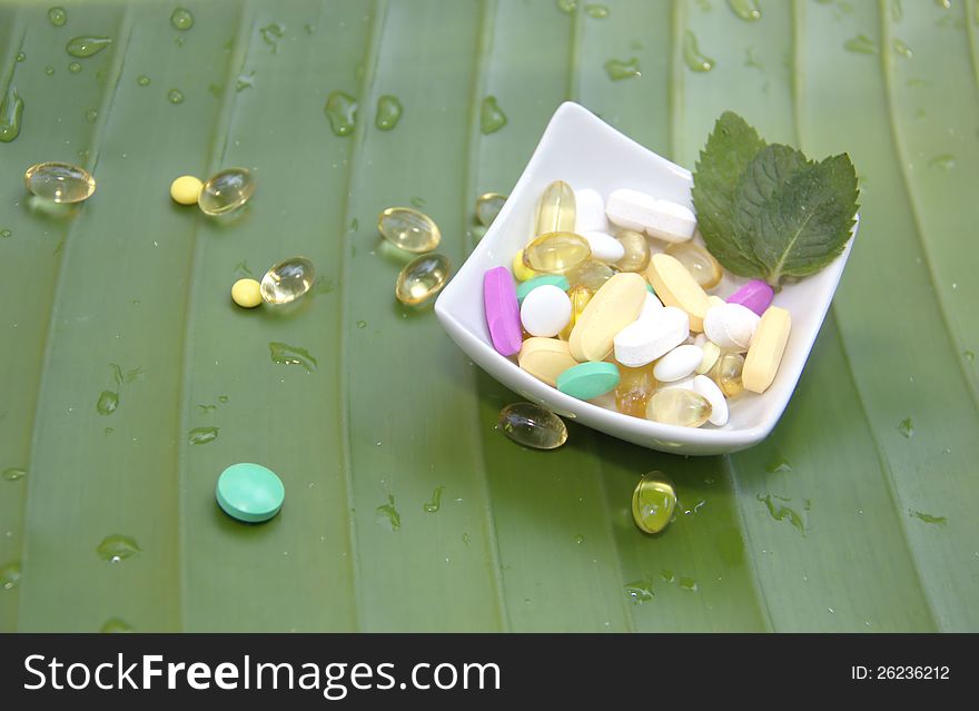 Assorted pills on green leaf background with drops of water. Assorted pills on green leaf background with drops of water