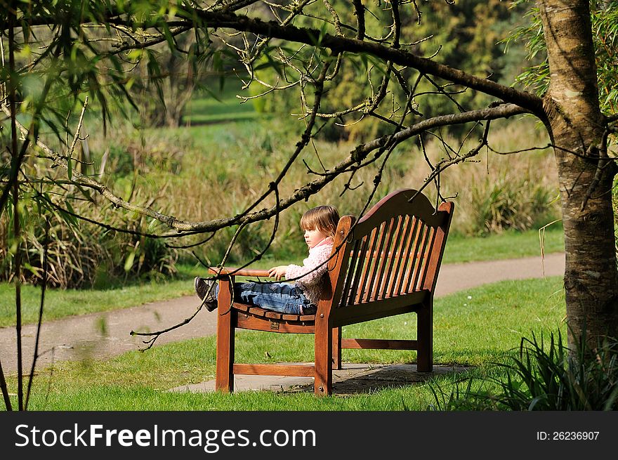 Little girl sitting on a bench in the park. Little girl sitting on a bench in the park