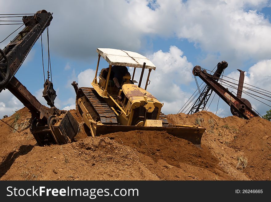 An old bulldozer pushing soil off the top of a huge stockpile. An old bulldozer pushing soil off the top of a huge stockpile.