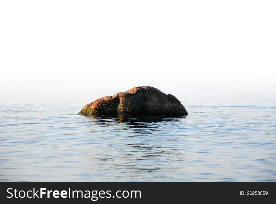 One big stone in tranquil sea under blank white space for text. One big stone in tranquil sea under blank white space for text