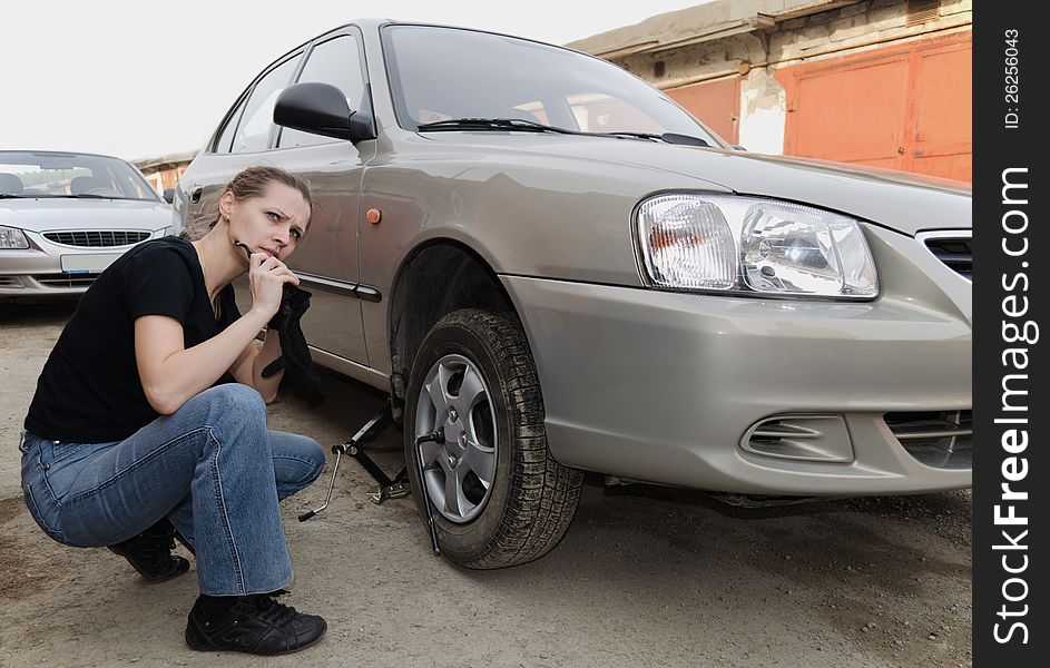 The beautiful young woman removes a wheel of the car near garage. The beautiful young woman removes a wheel of the car near garage