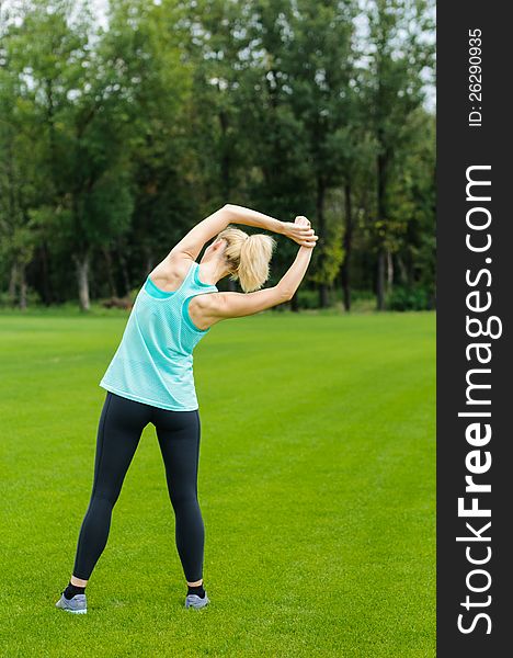 Woman doing overhead stretches as she is standing in the grass. Woman doing overhead stretches as she is standing in the grass