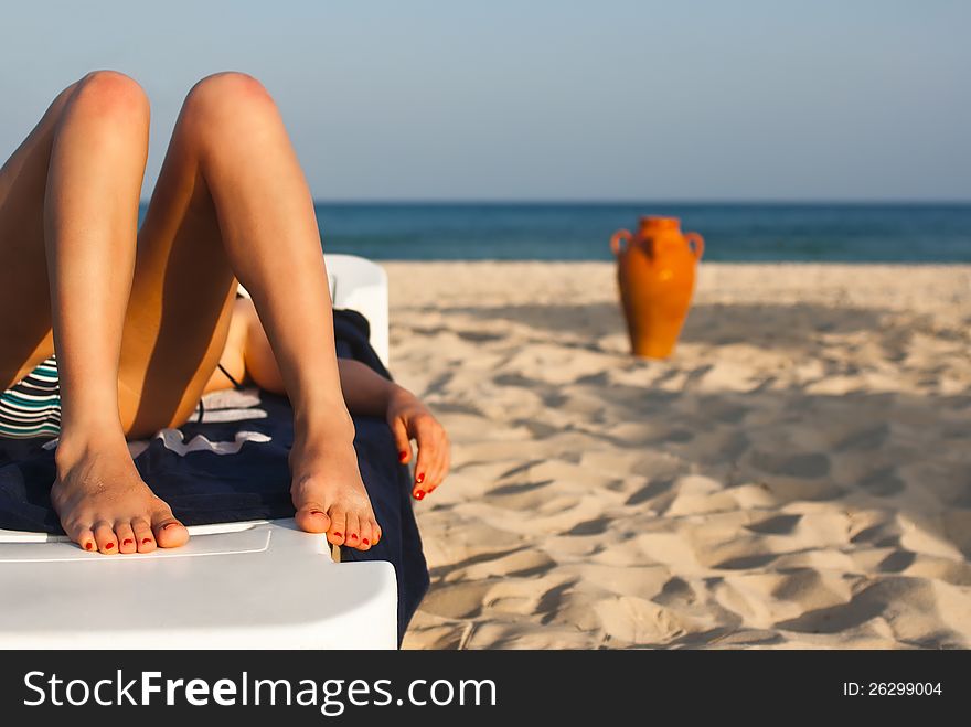 Legs of a beautiful woman relaxing on the beach with a amphora and the sea in the background. Legs of a beautiful woman relaxing on the beach with a amphora and the sea in the background