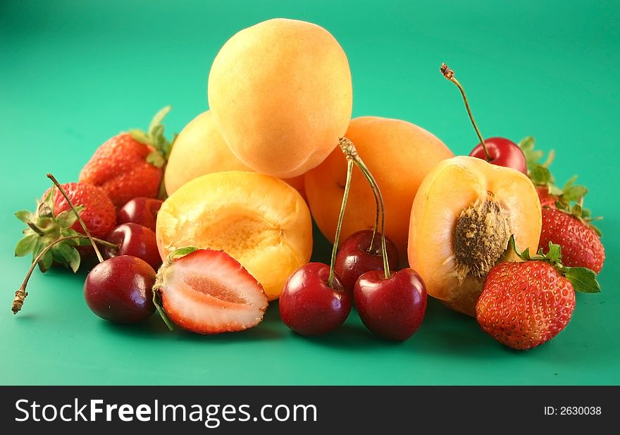 Apricots, sweet cherry  and strawberry is photographed on a green background. Apricots, sweet cherry  and strawberry is photographed on a green background