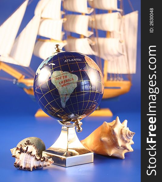 The globe and sea shells is photographed on a background of a sailing vessel