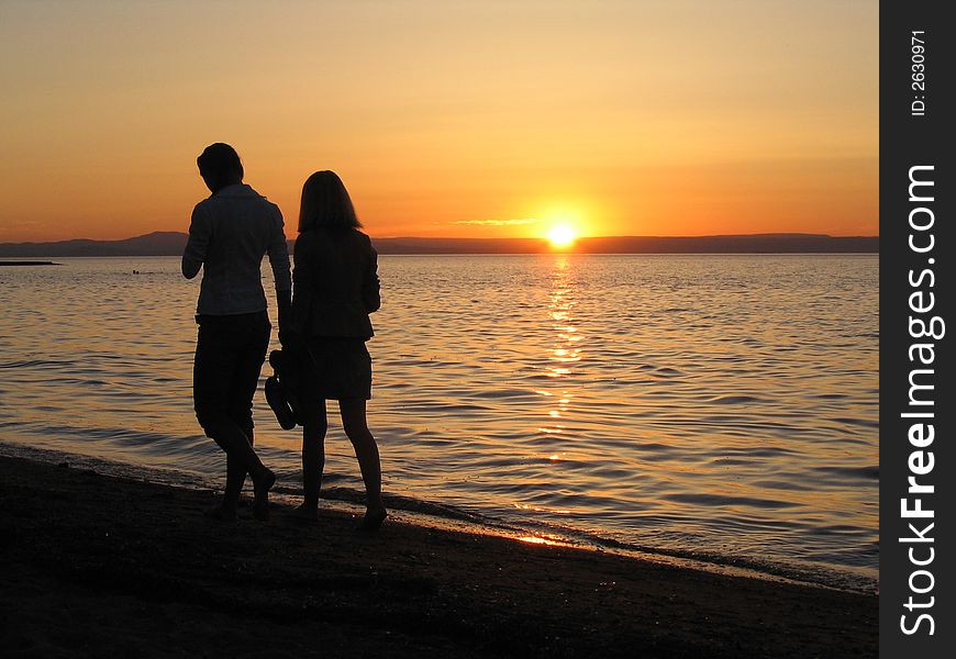 He and she walking near the sea at sunset