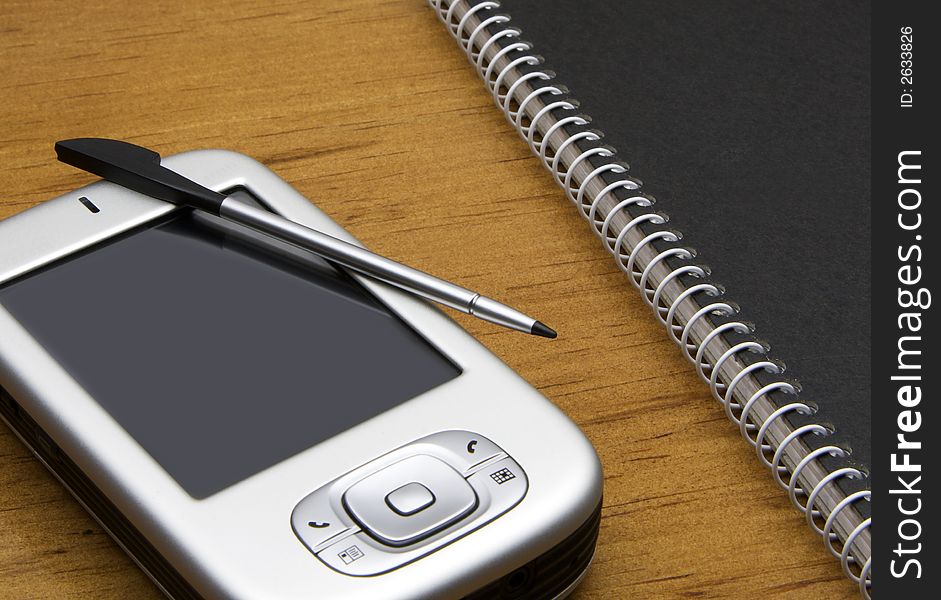 PDA with stylus lying on an office desk next to a ring-bound notebook. PDA with stylus lying on an office desk next to a ring-bound notebook