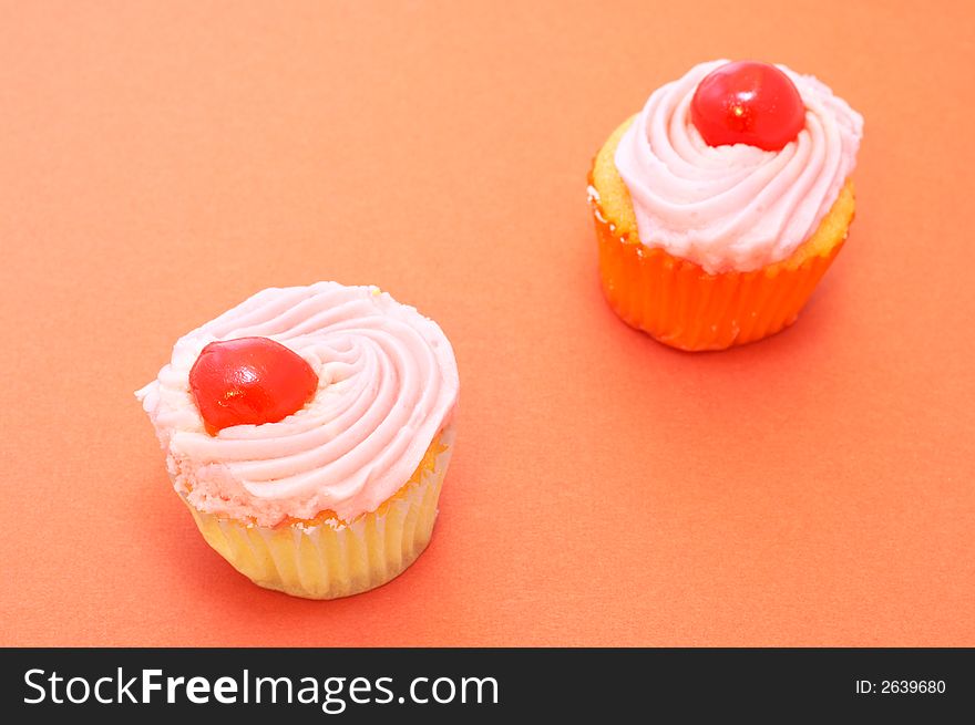 Two colorful vanilla cupcakes on orange paper background. Focus on front cupcake
