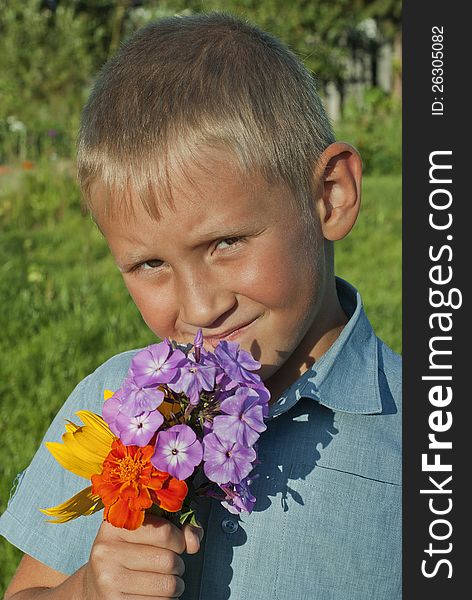 The serious boy of 6 years on a summer lawn holds a flower. The serious boy of 6 years on a summer lawn holds a flower