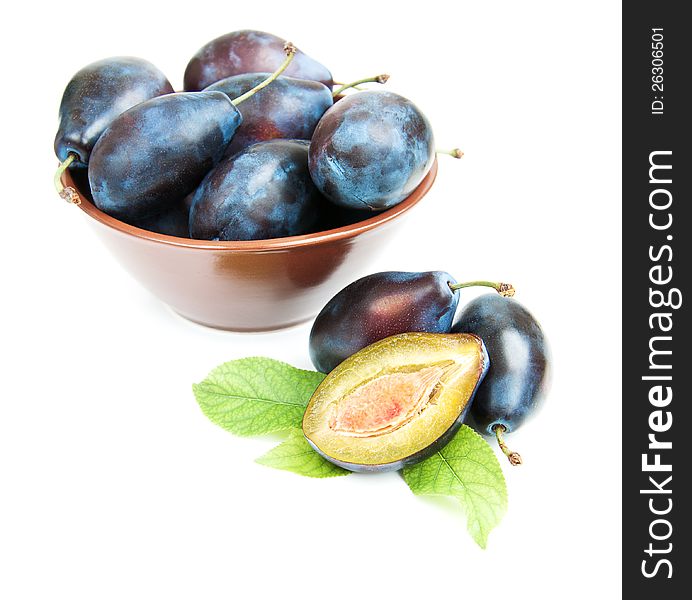 Bowl full of plums and  plus with green leaves   on a white background