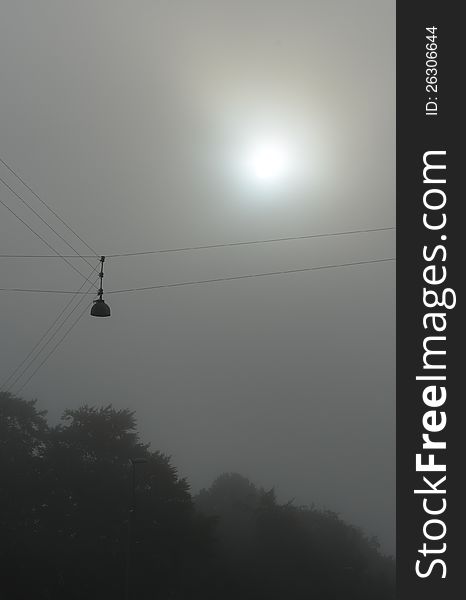 The receding autumn fog creates a near-monochrome contour of the city street lamp and trees against the blurred sun. The receding autumn fog creates a near-monochrome contour of the city street lamp and trees against the blurred sun.