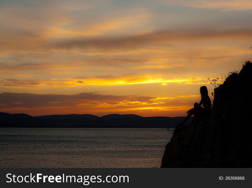 Girl sit on the marine stones at sundown. Girl sit on the marine stones at sundown