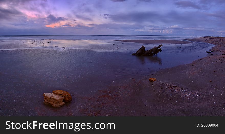 Beautiful decline on the sea coast, rock and snag on sand, majestic clouds, panorama