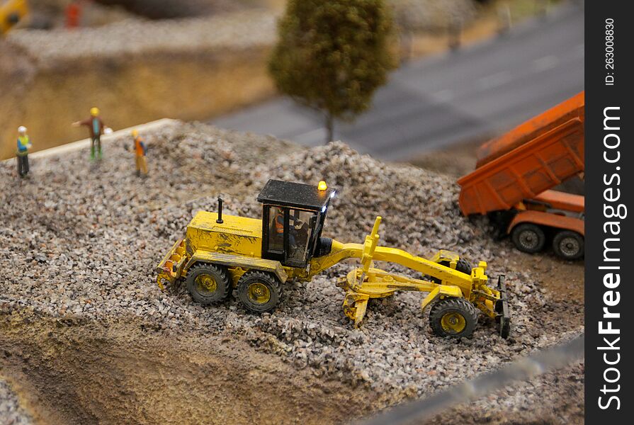 A small grader produsing tiny roadworks at toy maket of a town