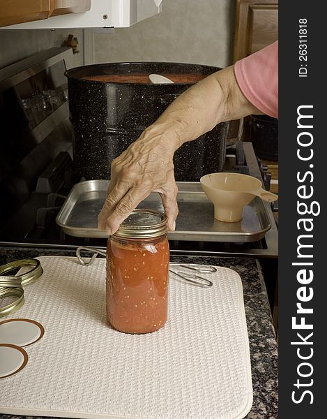 A woman screws the lid on a can of processed tomatoes as the final step in canning tomatoes. A woman screws the lid on a can of processed tomatoes as the final step in canning tomatoes.