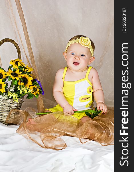 Baby girl sitting and smiling near the basket with flowers