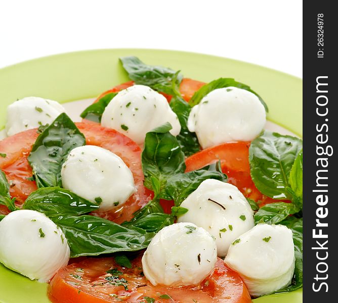 Italian Caprese Salad with Basil, Fresh Mozzarella, Tomatoes and Olive Oil on green plate close up on white background