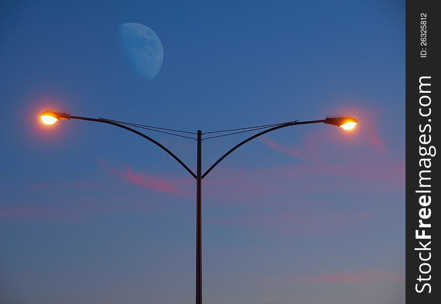 Streetlight glowing at the sunset with moon rising in the background. Streetlight glowing at the sunset with moon rising in the background