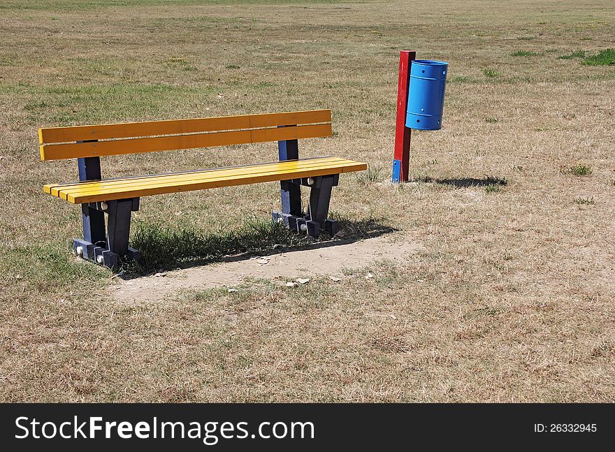 Yellow bench and blue recycle bin in the park