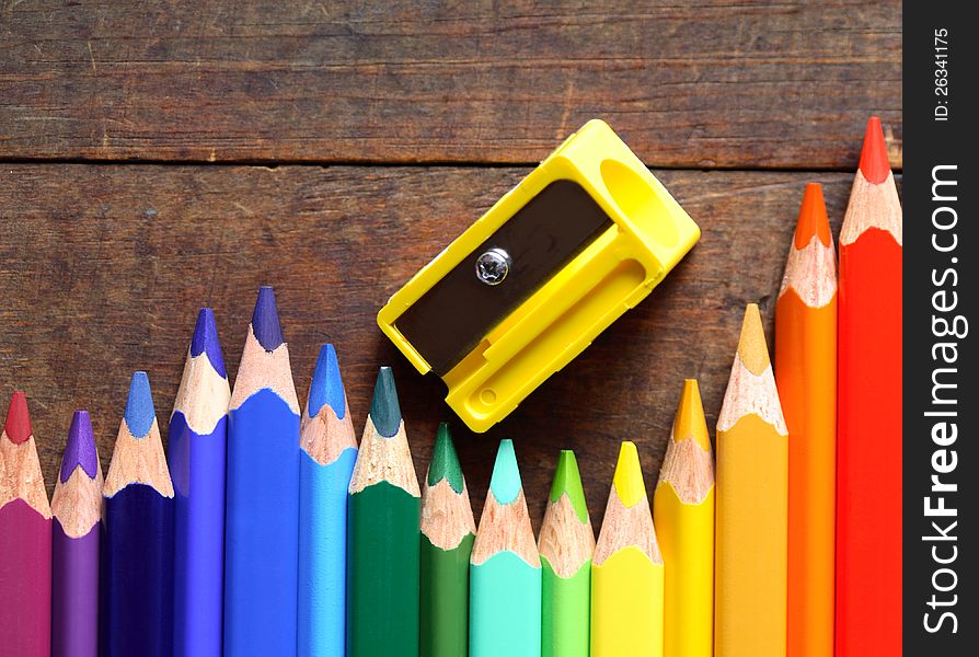 Closeup of variegated crayons in a row near pencil sharpener on wooden background