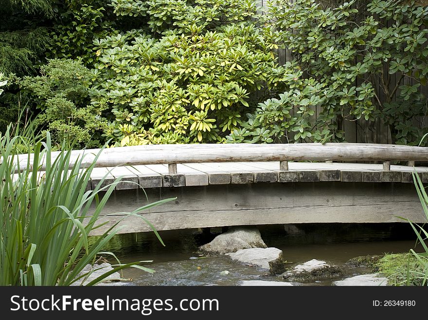 A wooden bridge hidden in the green in a Japanese garden. A wooden bridge hidden in the green in a Japanese garden
