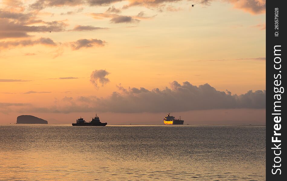 Cargo ships on the horizon of a quiet calm ocean in the dawn or sunset rays of the sun