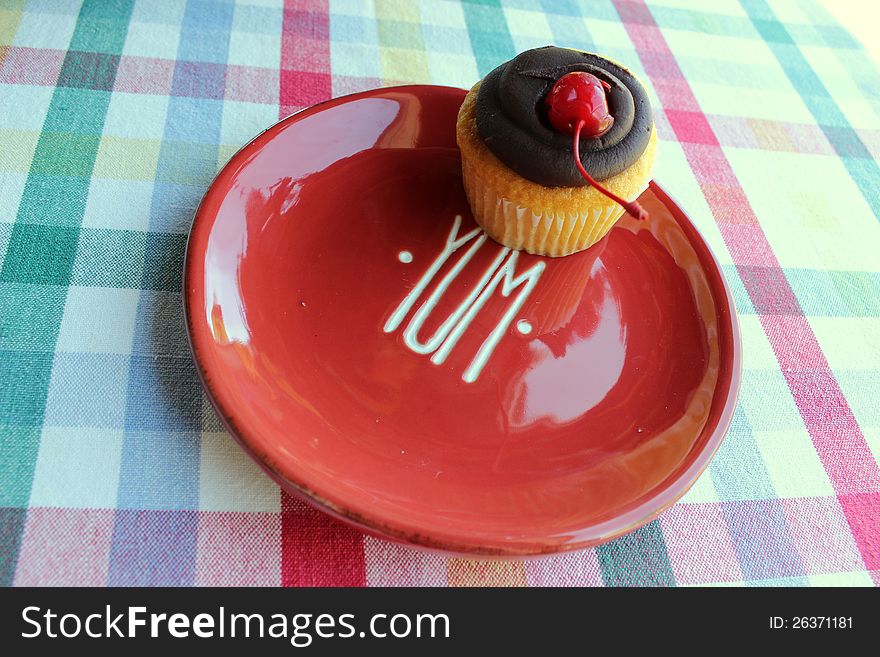 Colorful dessert plate with the word Yum and a boston creme cupcake on it,set on a nice patterned tablecloth. Colorful dessert plate with the word Yum and a boston creme cupcake on it,set on a nice patterned tablecloth.