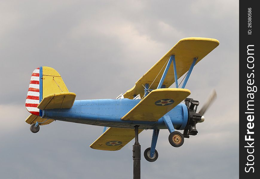 Weathervane with a yellow and blue single engine wooden bi-pane aircraft like a Stearman, against dark storm clouds. Weathervane with a yellow and blue single engine wooden bi-pane aircraft like a Stearman, against dark storm clouds.