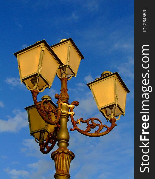 An antique lightpole. It stands rusty against the deep blue sky. Sardinia, Italy.