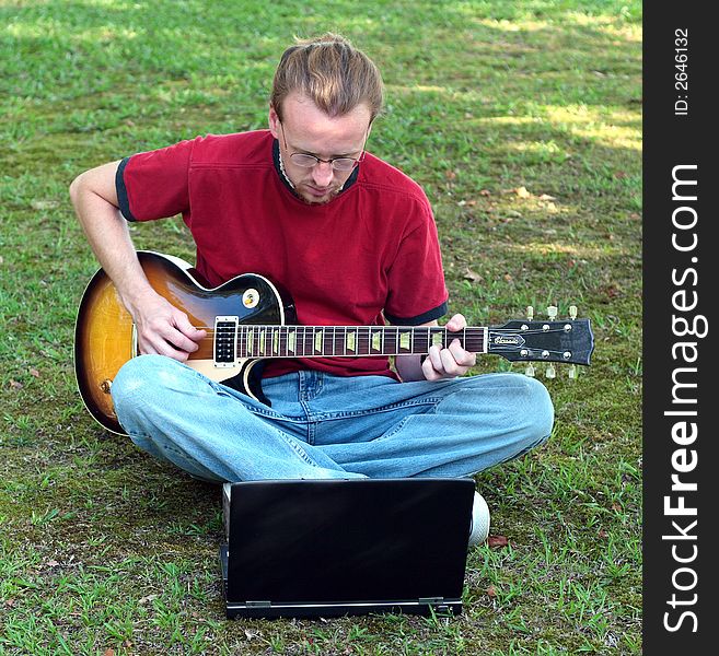 A guitarist plays in the out of doors with the assistance of his laptop. A guitarist plays in the out of doors with the assistance of his laptop.