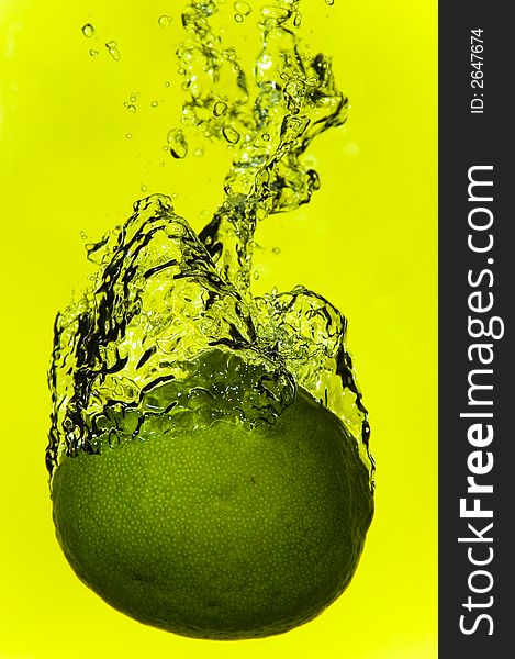 A lime plunging into water with a yellow background. A lime plunging into water with a yellow background
