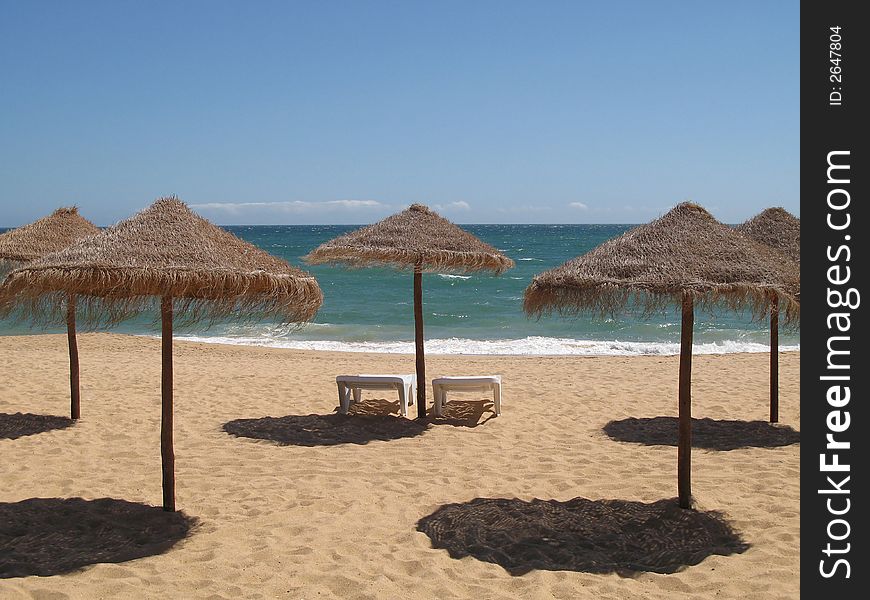 Two sun lounges and palm umbrellas on a beach. Two sun lounges and palm umbrellas on a beach