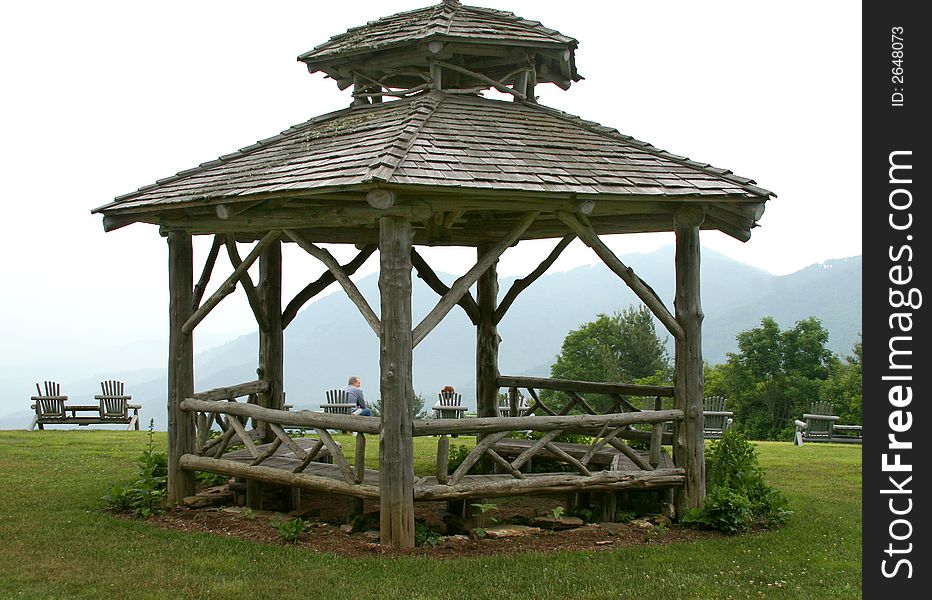 A rustic gazebo made of logs on a grassy mountain overlook. A rustic gazebo made of logs on a grassy mountain overlook